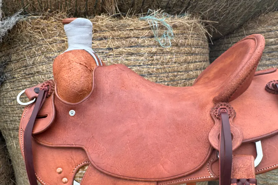 A roughout saddle with a one-piece covered swell, standing against hay bales