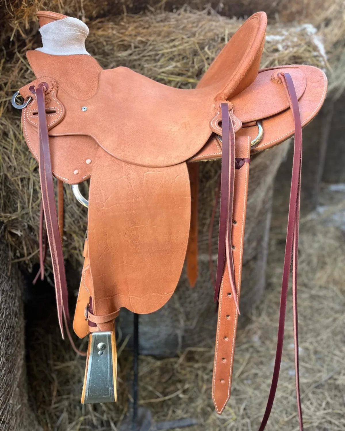Light veg-tan saddle on a rail in front of a haystack