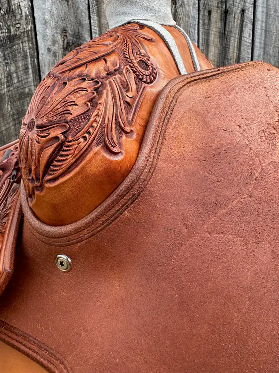 Hand-carved floral cantle above a roughout skirt on a working saddle