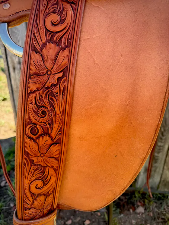 Close-up of a hand-carved floral fender against the smooth skirt of a saddle