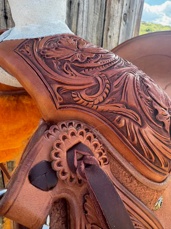 Hand-carved scrollwork and leaves on a saddle fender, photographed outdoors