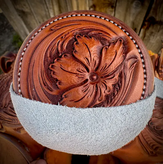 Hand-carved floral horn cap with a beaded border on a finished saddle