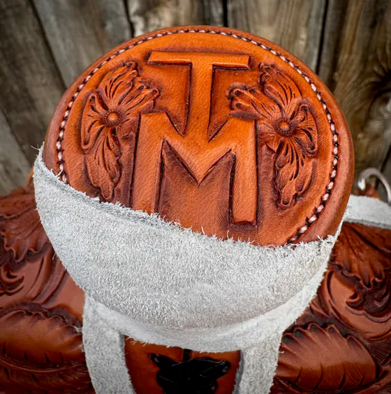 Saddle horn cap carved with a TM brand flanked by two hand-cut flowers