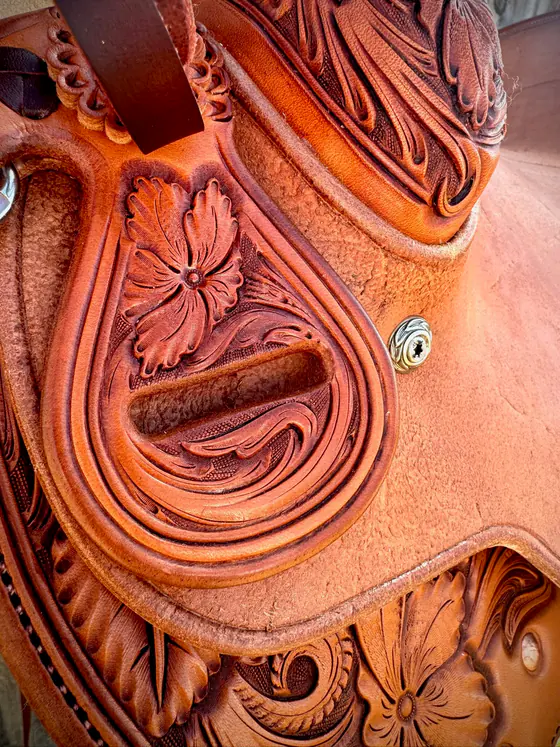 Detail of a carved saddle jockey and stirrup leather slot with a silver concho