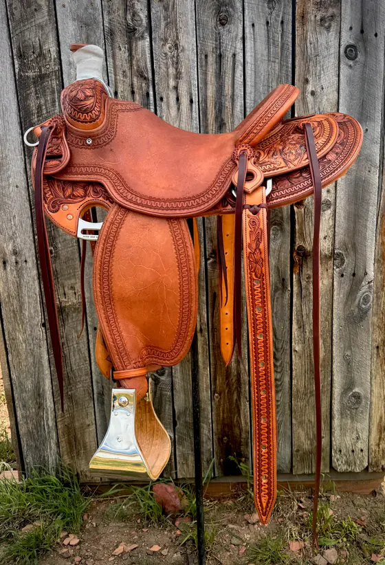 Full side view of a custom saddle with hand-stamped borders and floral corner tooling