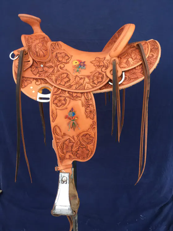 Full floral-carved custom saddle with small hand-painted flowers on the seat and fender, against a blue backdrop