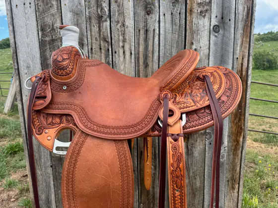 Custom saddle with geometric border stamping and carved floral corners against a plank wall