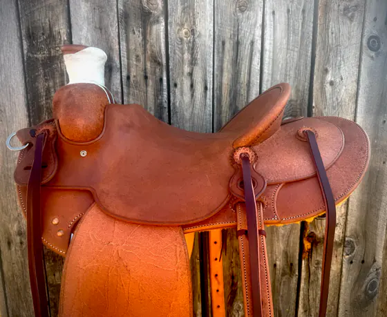 Plain roughout ranch saddle built for everyday work, hung against weathered boards
