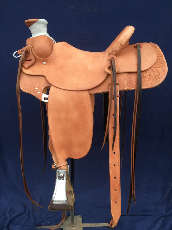 Plain roughout slick-fork custom saddle on a stand against a blue backdrop