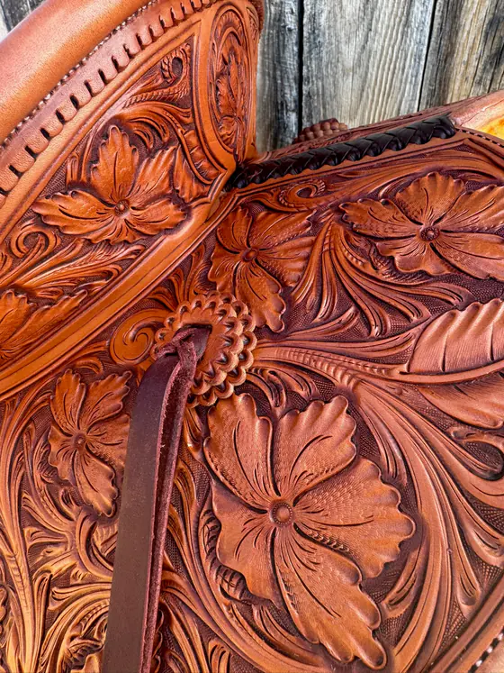 Close view of deep-cut floral carving across a saddle seat and cantle
