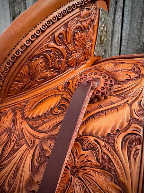 Engraved silver corner plate set into deeply carved floral tooling on a saddle