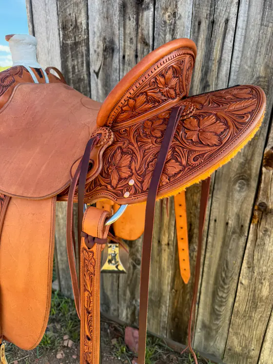 Floral-tooled saddle skirt and jockey photographed against weathered wood