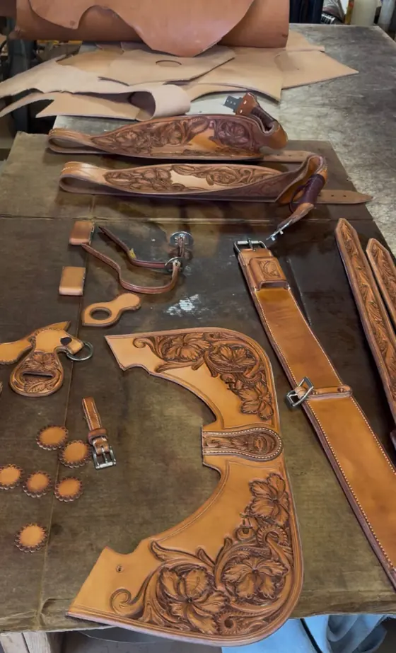 A set of hand-tooled saddle and tack parts laid out on the bench before assembly