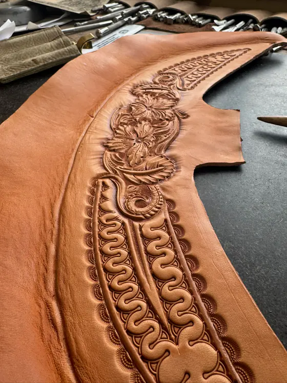 A saddle skirt part-way through carving, showing floral and border work in progress