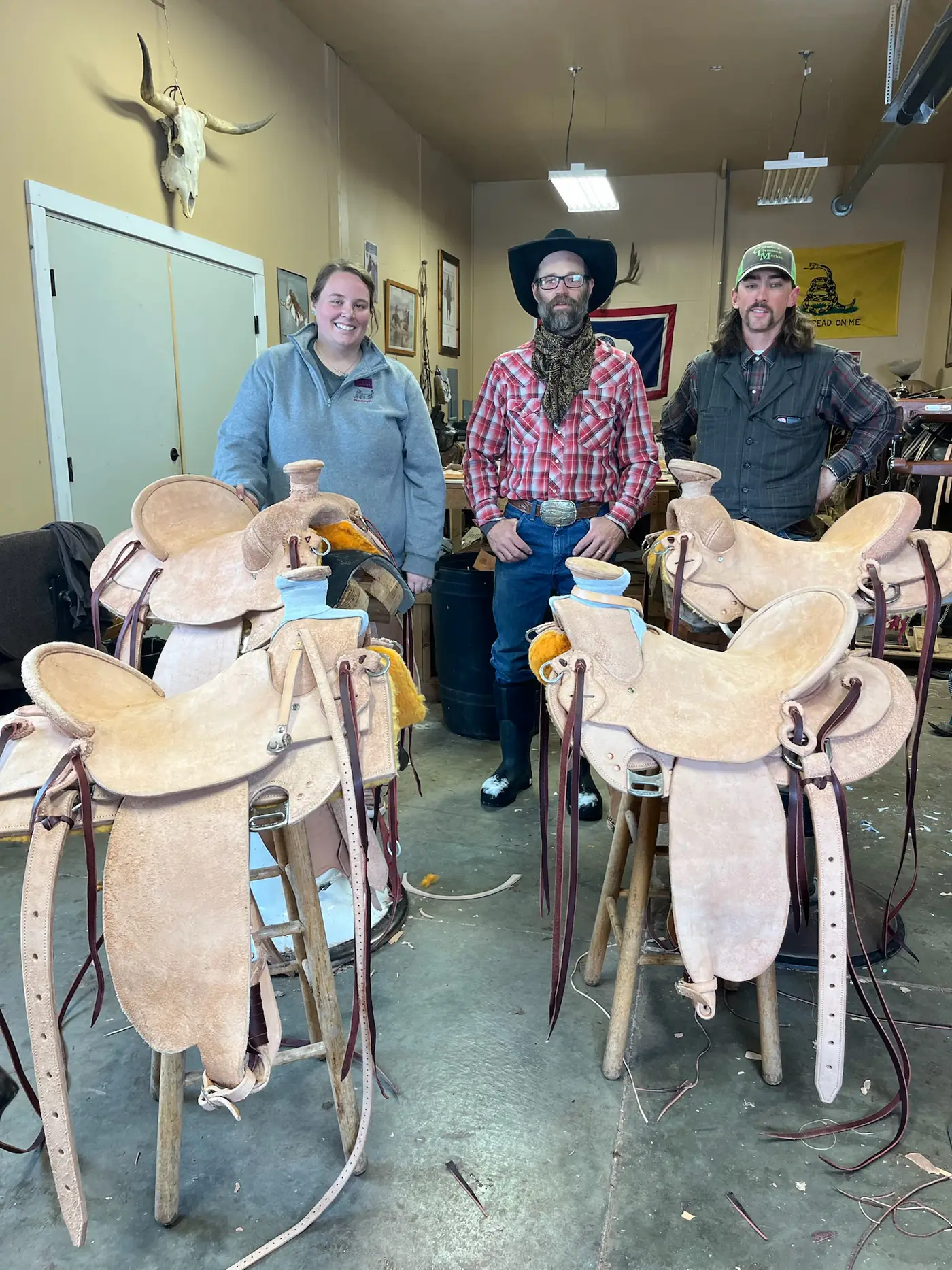 Paul Van Dyke in the Sheridan shop with two students and the saddles they built