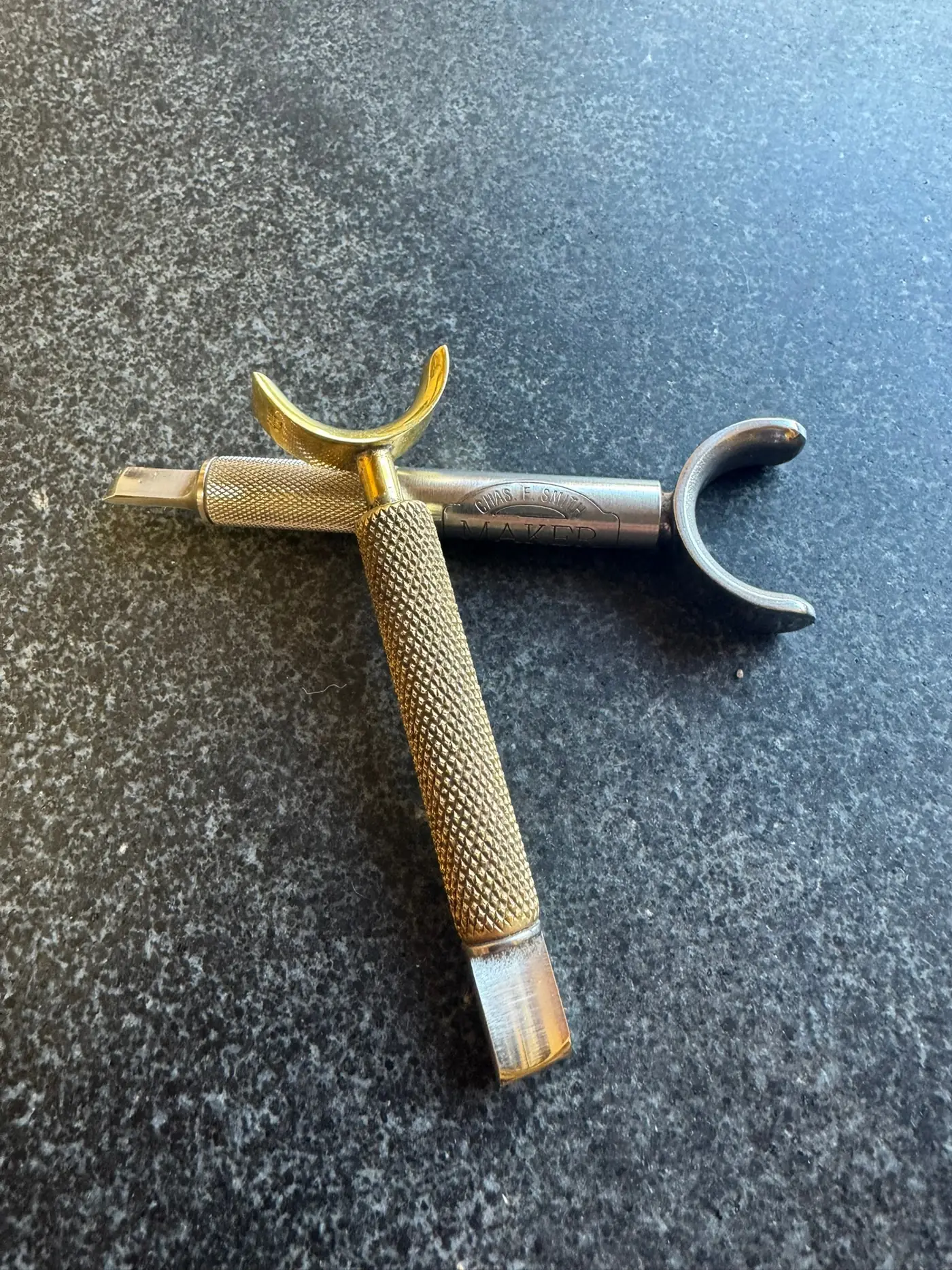 A saddler's swivel knife with a knurled barrel and brass yoke resting on the bench